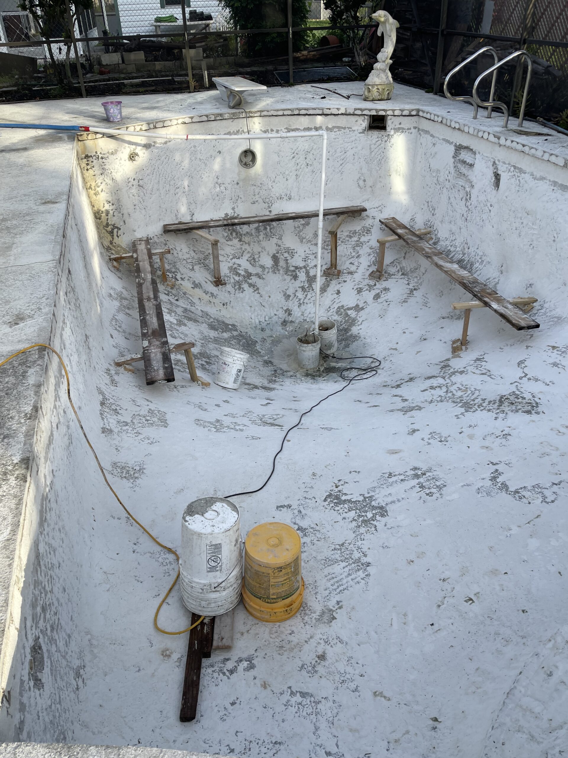 A person cleans a pool using a hose and a bucket, removing debris and maintaining water clarity.