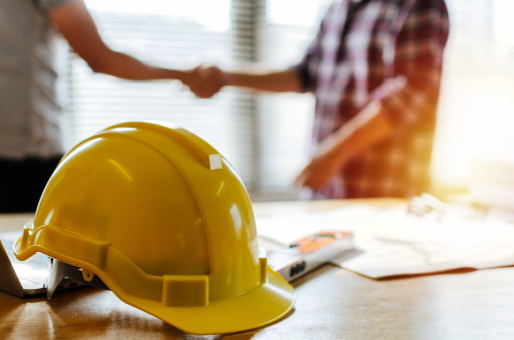 construction worker team hands shaking greeting start up plan new project contract behind yellow safety helmet on workplace desk in office center at construction site